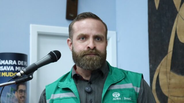 Diretor estadual da ADRA com colete verde e barba, posicionado diante de um microfone em sessão na Câmara Municipal
