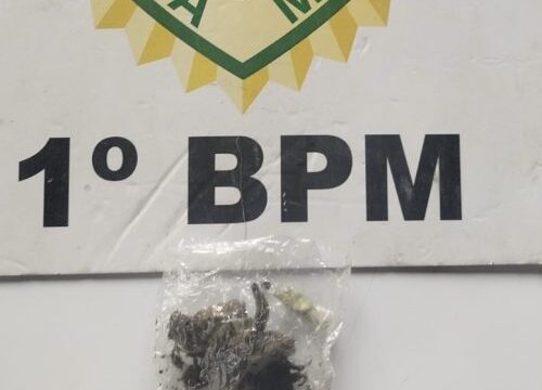 Porção de maconha em saquinho plástico transparente sobre fundo com o emblema da Polícia Militar e a identificação do 1º BPM