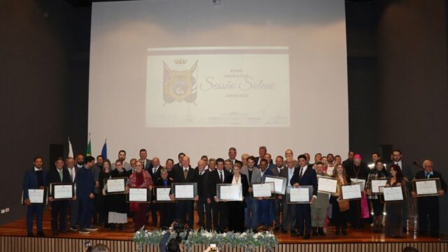 Grupo de pessoas posando no palco com certificados durante sessão solene em Ponta Grossa
