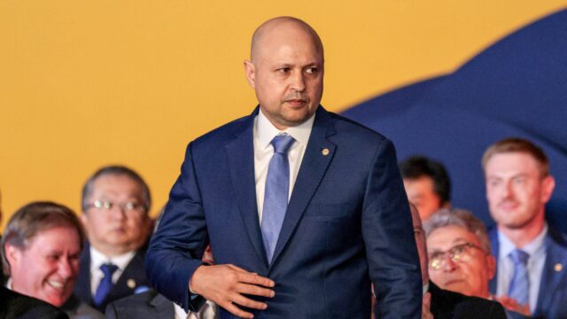 Edson Vasconcelos de terno azul em evento com plateia ao fundo