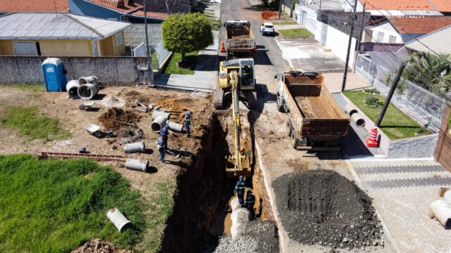 Vista aérea de obra da Prefeitura de Ponta Grossa com escavadeira em valeta na rua