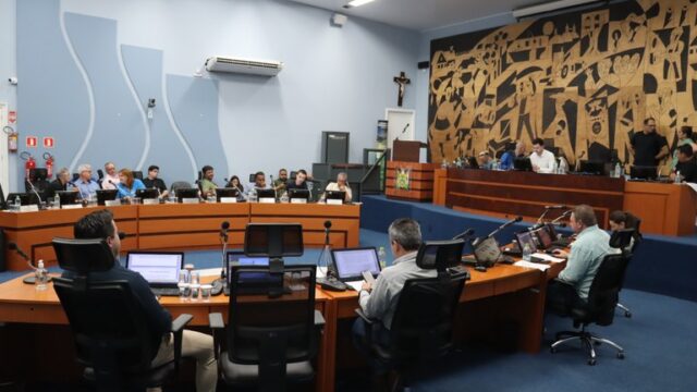 Vereadores sentados em mesas semicirculares no plenário da Câmara Municipal de Ponta Grossa durante sessão