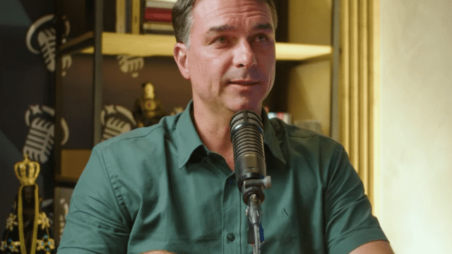 Senador Flávio Bolsonaro com camisa verde escura falando ao microfone em estúdio