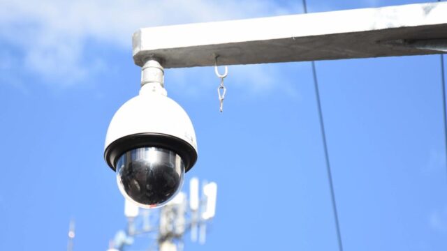 Câmera de segurança tipo domo instalada em suporte metálico contra o céu azul
