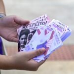 Pessoa com blusa roxa segura leque de panfletos informativos e lixas de unha com mensagens de apoio