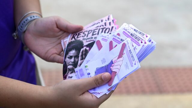 Pessoa com blusa roxa segura leque de panfletos informativos e lixas de unha com mensagens de apoio