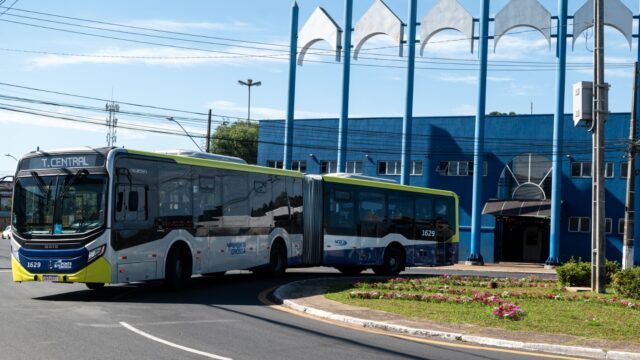 Ônibus articulado de transporte coletivo em rua de Ponta Grossa com prédio azul ao fundo