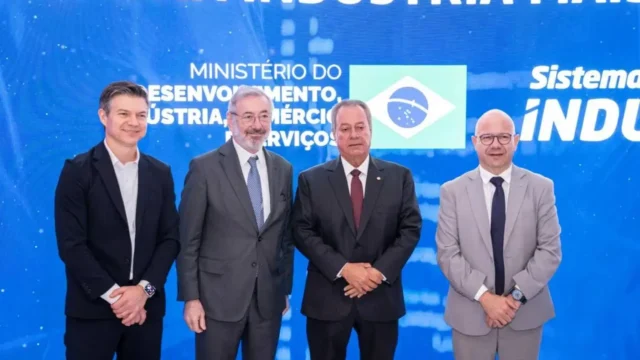 Quatro autoridades em pé e de terno posam para foto diante de painel azul com inscrições do Ministério