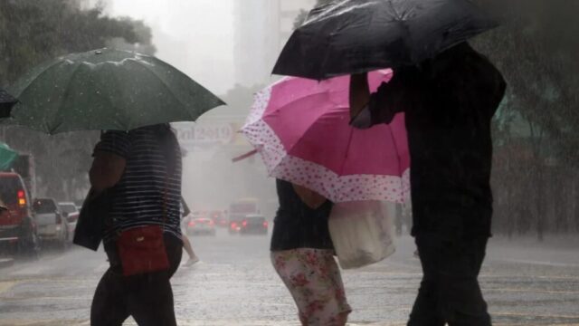 Pedestres andam sob forte chuva na rua utilizando guarda-chuvas durante temporal