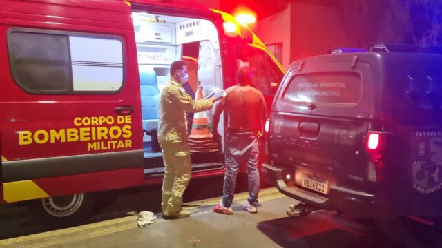 Homem sem camisa recebendo atendimento de bombeiro militar em viatura durante a noite