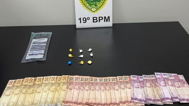 Dinheiro em notas e porções de drogas sobre uma mesa com placa do 19º BPM da Polícia Militar do Paraná