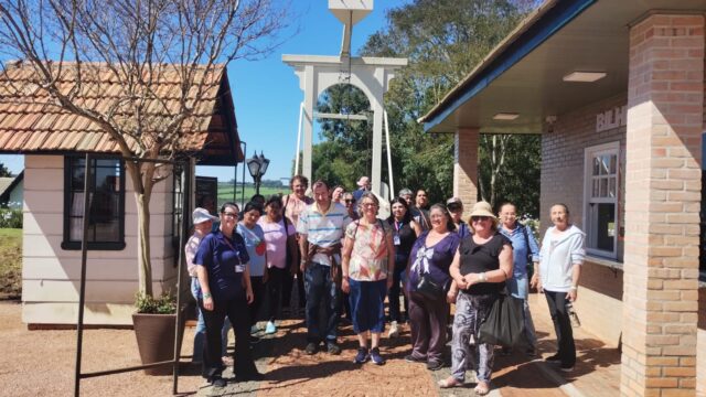 Grupo de visitantes em pé em uma praça pavimentada com construções históricas ao fundo