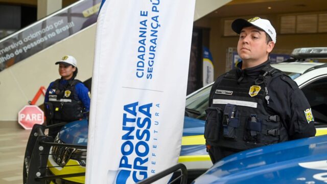 Agentes de trânsito fardados com bonés e viaturas em exposição durante evento em shopping