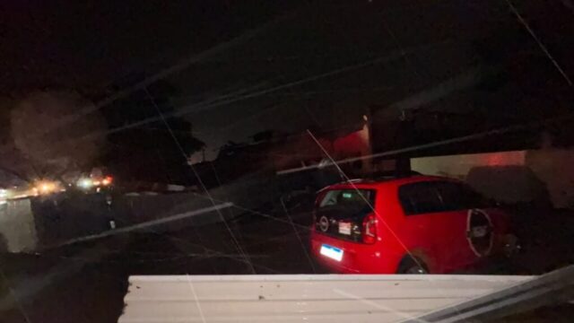 Carro vermelho danificado e telhado arrancado por tempestade no Paraná à noite