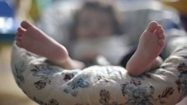 Pés de um bebê em destaque sobre um travesseiro acolchoado com fundo desfocado