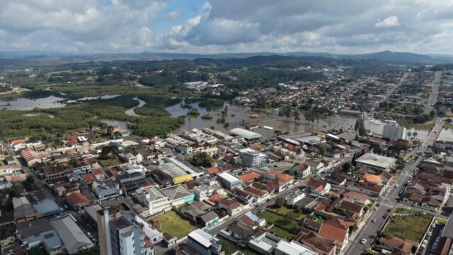 Vista aérea de área urbana e região alagada com construções e vegetação em Castro, Paraná