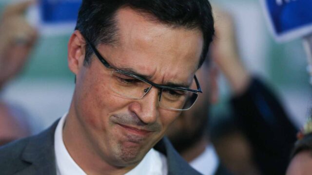 Primeiro plano do rosto de Deltan Dallagnol usando óculos com armação preta e terno cinza