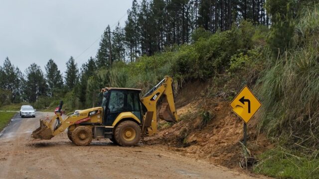 Trator retroescavadeira limpa pista com terra de deslizamento em rodovia