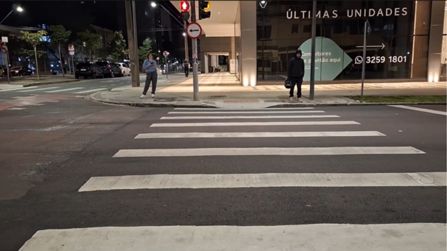 Faixa de pedestres em rua asfaltada à noite com edifícios e iluminação pública ao fundo