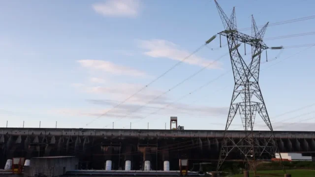 Torre de alta tensão e estrutura de usina hidrelétrica sob céu azul e limpo
