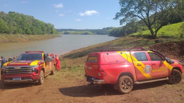 Duas caminhonetes do Corpo de Bombeiros na margem de terra de uma represa sob céu azul