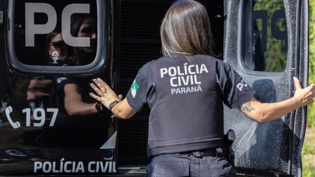 Policial feminina da Polícia Civil do Paraná em pé ao lado de viatura policial