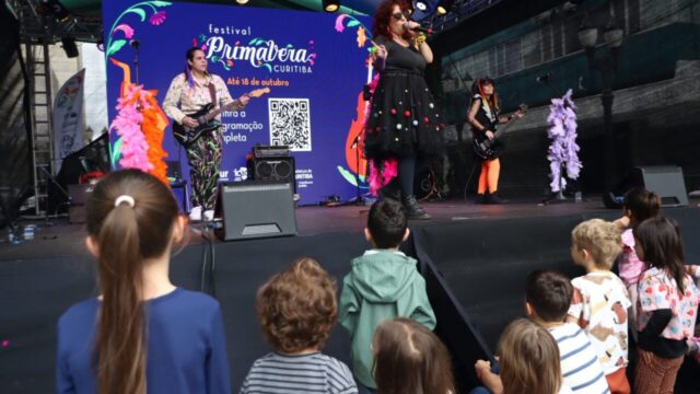 Crianças assistem a show musical no Palco das Flores com banda tocando ao fundo
