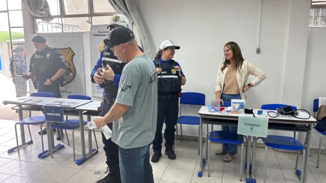 Agentes de segurança pública e trânsito conversam com visitantes junto a mesas informativas na Feira das Profissões na UEPG