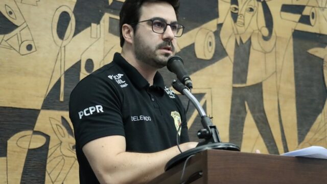 Delegado de óculos com camisa preta da Polícia Civil discursa em tribuna na Câmara Municipal