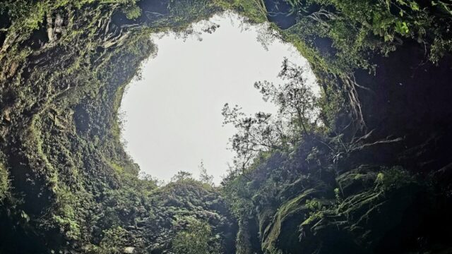Interior de furna rochosa com abertura circular no teto permitindo a entrada de luz e vegetação nas paredes