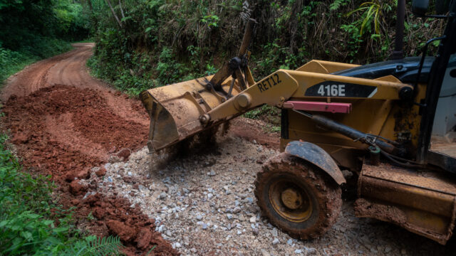Trator retroescavadeira realizando manutenção com aplicação de cascalho em estrada rural