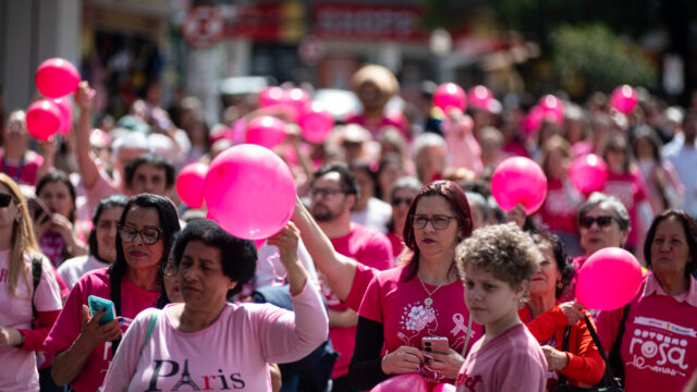 Multidão com camisas e balões cor-de-rosa caminha pela rua durante evento de conscientização no centro