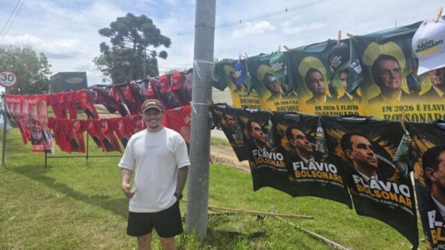 Homem em pé em gramado próximo a varal ao ar livre exibindo camisetas políticas à venda em Curitiba