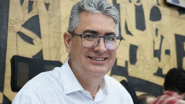 Homem de óculos e camisa xadrez sorrindo em ambiente interno