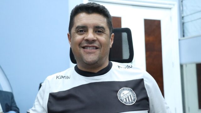 Homem sorridente vestindo camisa branca e preta do Operário Ferroviário em ambiente interno