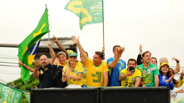 Flávio Bolsonaro acenando para apoiadores de cima de um carro de som vestindo camisa amarela