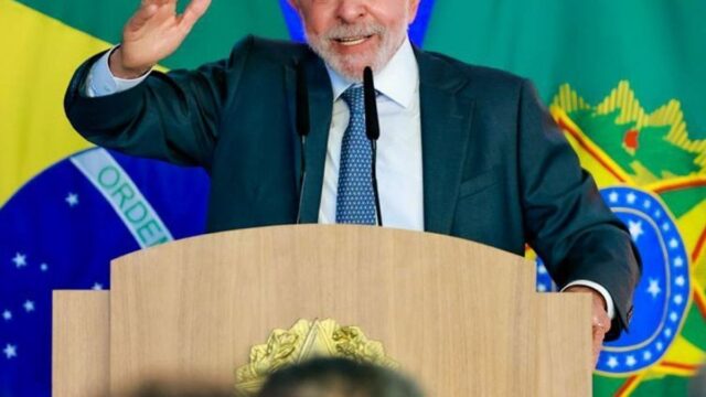 O presidente Luiz Inácio Lula da Silva gesticula atrás de um púlpito com bandeiras do Brasil ao fundo