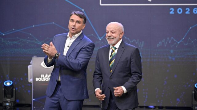Flávio Bolsonaro e Lula sorriem lado a lado no estúdio durante debate presidencial na Band