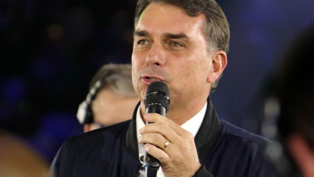 Flávio Bolsonaro discursa segurando um microfone durante evento político