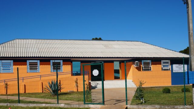 Fachada frontal do prédio do CRAS Costa Rica com paredes laranjas e portão de metal verde em Ponta Grossa