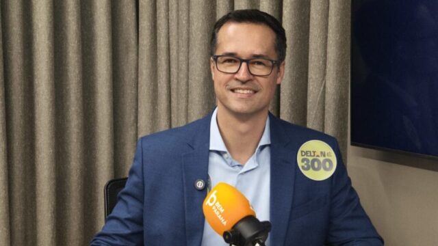 Deltan Dallagnol usando óculos, camisa azul clara e terno azul durante entrevista em estúdio