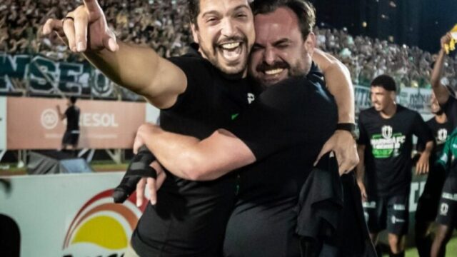 Dois dirigentes do Maringá FC abraçados e sorrindo intensamente no gramado durante comemoração