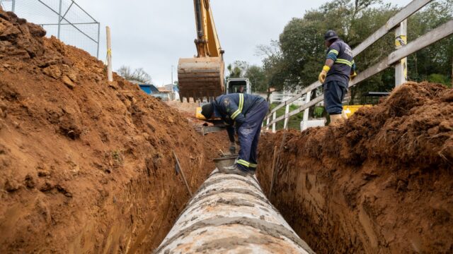 Obreiros trabalham na instalação de tubos de concreto em vala profunda de drenagem urbana em Ponta Grossa