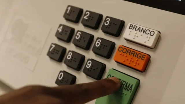 Eleitor votando em urna eletrônica com teclado numérico e teclas branco, corrige e confirma