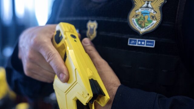 Agente da Guarda Civil de Ponta Grossa manuseia equipamento de segurança amarelo em uniforme escuro