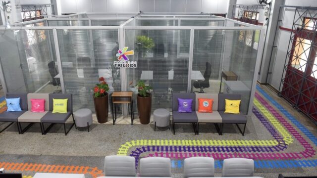 Ambiente interno de escritório com divisórias de vidro, mesas de trabalho e poltronas coloridas