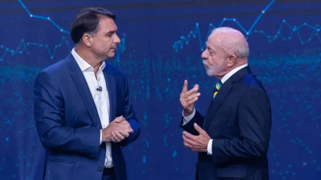 Flávio Bolsonaro e Lula gesticulam durante debate ou encontro político com fundo azul