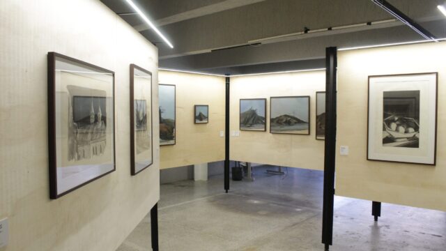 Salão de exposição com quadros e gravuras emoldurados em paredes de madeira