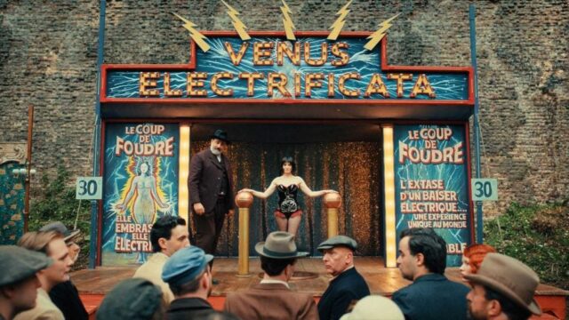 Palco de show com letreiro luminoso 'Venus Electrificata' e espectadores assistindo à apresentação