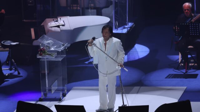 Roberto Carlos com terno branco no palco do Teatro Positivo segurando o microfone